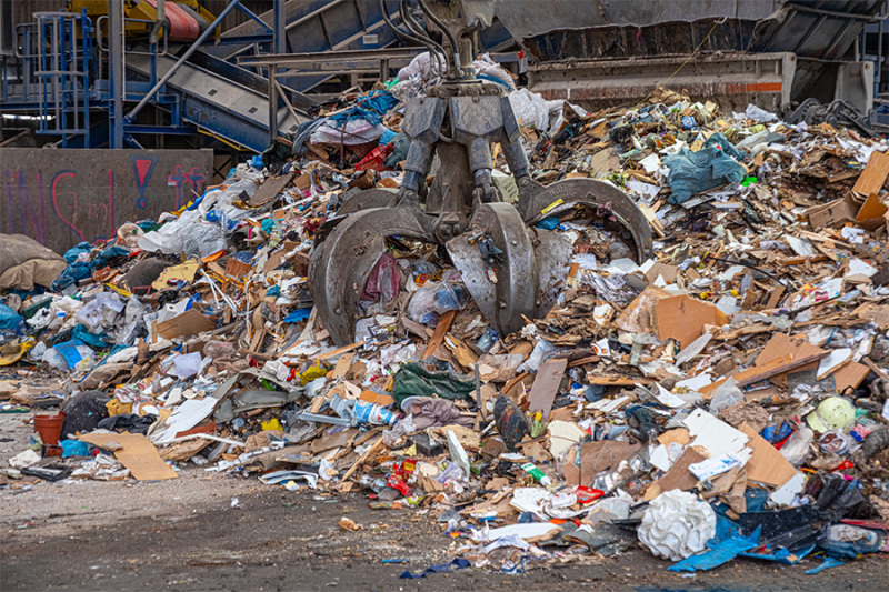 Klaue vom Bagger greift einen Haufen Müll.
