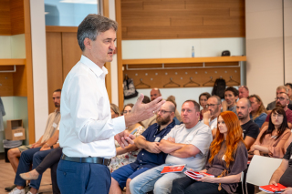 Der Vorsitzende der Geschäftsführung, Matthias Lux, steht im Raum vor den neuen Mitarbeiterinnen und Mitarbeitern und stellt das Unternehmen vor.
