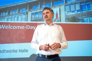 Der Vorsitzende der Geschäftsführung, Matthias Lux, steht im Raum vor den neuen Mitarbeiterinnen und Mitarbeitern und stellt das Unternehmen vor.